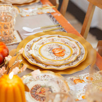 Create a festive autumn table with the Sophistiplate Turkey & Gourds Table Setting, featuring designer plates, gold utensils, elegant glassware, and pumpkin décor in warm orange, gold, and neutral tones.