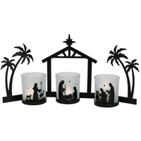 black metal nativity set featuring the Christmas star, palm trees on either side of the stable and attached candle holders with black metal silhouette nativity scenes around glass cup